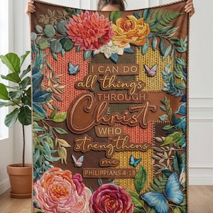 May include: A decorative throw blanket featuring floral and butterfly designs with the text "I can do all things through Christ who strengthens me." The blanket has a brown border and a patchwork design with various colors.
