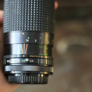 Może przedstawiać: Czarny obiektyw do aparatu z srebrnym pierścieniem i oznaczeniami ustawień przysłony, w tym 1,8, 2, 6 i 7. Obiektyw ma r&oacute;wnież ustawienie makro.