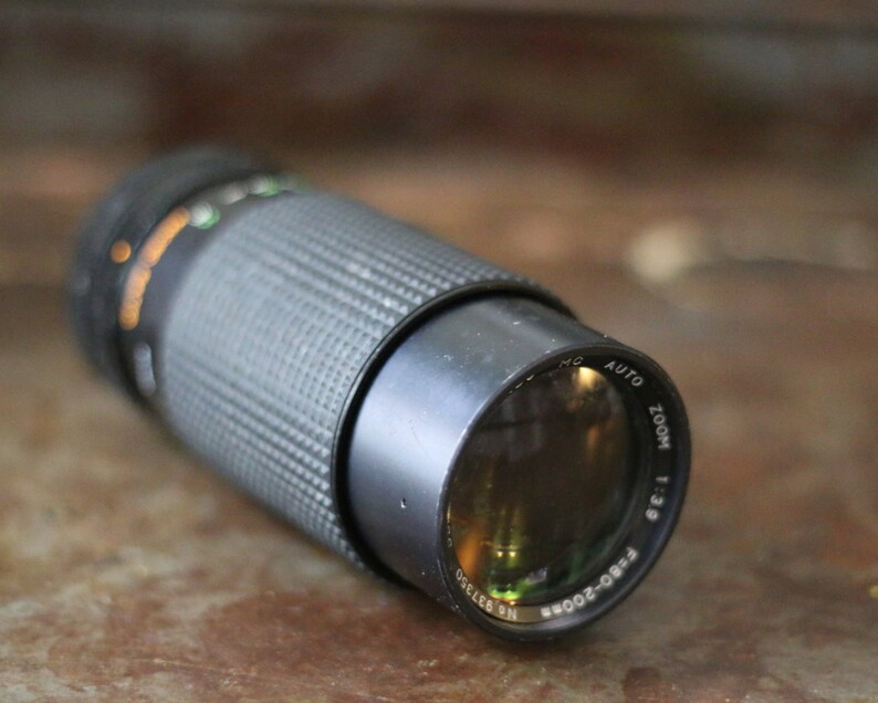 Może przedstawiać: Czarny obiektyw do aparatu z srebrnym pierścieniem i nadrukiem "RBO-2000R ZOOM 1:3.9 AUTO" na boku.