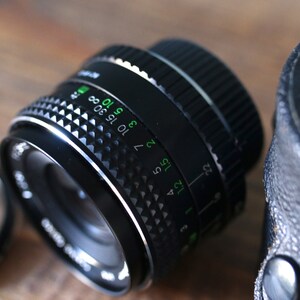 May include: A black camera lens with a silver ring and a depth of field scale marked in green. The scale shows numbers from 1.2 to 22 and 3 to 30.