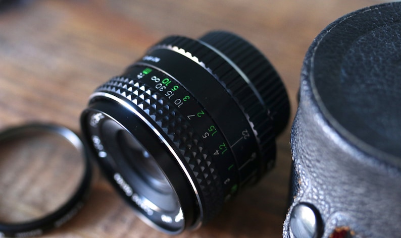 May include: A black camera lens with a silver ring and a depth of field scale marked in green. The scale shows numbers from 1.2 to 22 and 3 to 30.