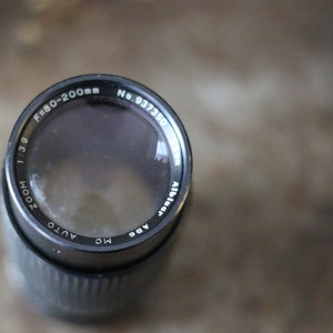 Może przedstawiać: Czarny obiektyw do aparatu z nadrukiem "ZOOM 1:3.9 F=80-200mm AUTO MC ADE" i "No. 937350" na boku.