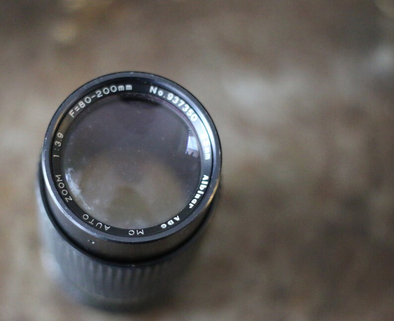 Może przedstawiać: Czarny obiektyw do aparatu z nadrukiem "ZOOM 1:3.9 F=80-200mm AUTO MC ADE" i "No. 937350" na boku.