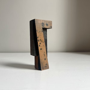 May include: A vintage wooden number seven block with a distressed appearance. The block is primarily light brown with black ink splatters and accents. The number has a unique, angular design, and is likely used for printing or display.