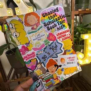 May include: A rectangular sticker sheet featuring a collage of 90s-themed illustrations and text. Graphics include cartoon characters, a library card, a flip phone, and text reading Chasing that Scholastic Book Fair high, 90's Kid, and Big book energy.
