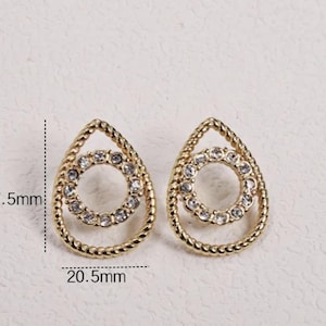 Peut inclure: Boucles d'oreilles dorées en forme de goutte d'eau avec un motif de corde texturée. Chaque boucle d'oreille comporte un cercle central de cristaux transparents et mesure environ 27,5 mm de hauteur et 20,5 mm de largeur. Accessoire élégant.