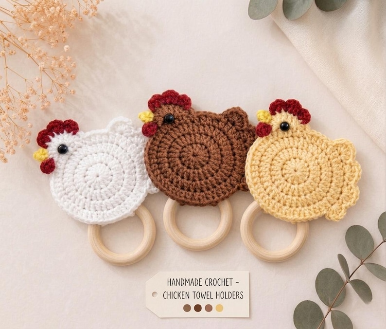 May include: Three handmade crochet chicken towel holders with wooden rings. The chickens are white, brown, and light yellow, each featuring a red comb, yellow beak, and black eye. A rectangular tag reads: HANDMADE CROCHET - CHICKEN TOWEL HOLDERS.