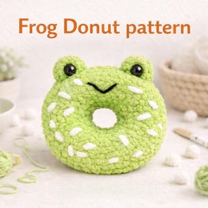 May include: A green crochet frog-shaped donut with white spots and black eyes. The text "Frog Donut pattern" is displayed above the donut. The image includes balls of yarn, a bowl, and a basket.