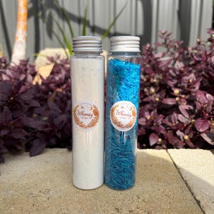 May include: Two clear plastic tubes with silver screw-on caps. One tube is filled with a fine white powder, and the other contains bright blue grains. Each tube features a circular white label with the text Whimsy Kids and a botanical design.