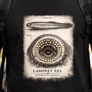 May include: A black t-shirt featuring a vintage-style scientific illustration of a lamprey eel. The graphic includes a side view labeled Fig. A, a detailed close-up of the circular mouth labeled Fig. B, and the text LAMPREY EEL PETROMYZON MARINUS.