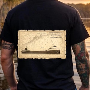 May include: Black t-shirt featuring a vintage-style map of Lake Superior and the SS Edmund Fitzgerald bulk freighter. The map includes the date November 10, 1975. The shirt has a classic, nautical theme.