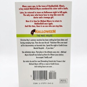 May include: The back cover of a book titled "Halloween: The Mad House", detailing a horror story about Michael Myers. The cover has a green and orange banner with the title and a knife graphic.