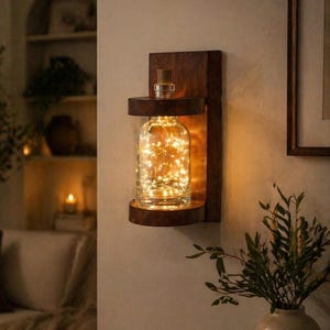May include: A wall-mounted light fixture with a clear glass bottle filled with warm white LED lights. The bottle sits in a dark brown wooden frame. The fixture is designed to hold the bottle upright, creating a warm and inviting atmosphere.