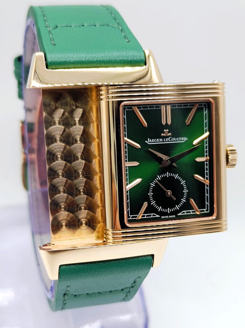 Puede incluir: Un reloj de pulsera rectangular dorado con esfera verde y un peque&ntilde;o dial de segundos. El reloj tiene una correa de cuero verde. La marca "JAEGER-LECOULTRE" es visible en la esfera. El reloj est&aacute; marcado "SWISS MADE".