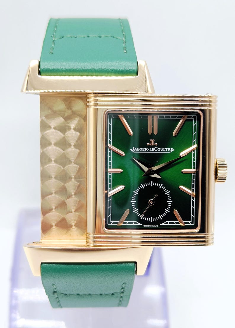 Puede incluir: Un reloj Jaeger-LeCoultre dorado con esfera verde y correa de cuero verde. El reloj tiene una esfera rectangular con agujas e indicadores dorados. La correa mide aproximadamente 2 cm de ancho.
