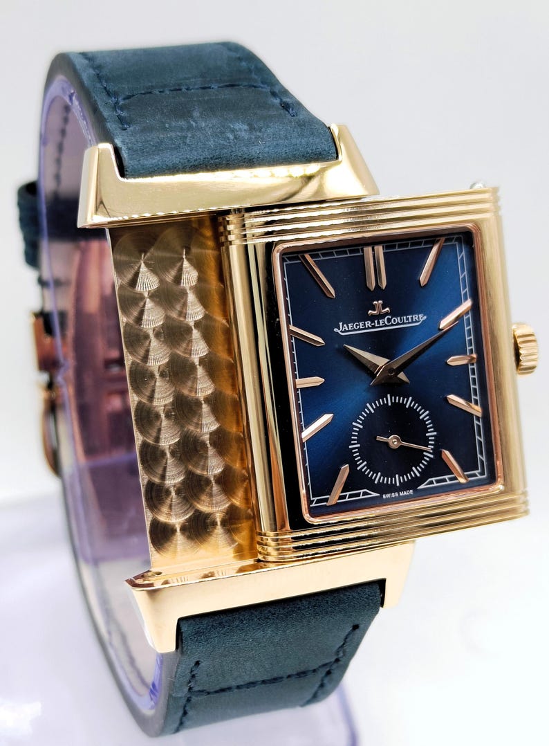 K&ouml;nnte beinhalten: Eine goldfarbene Jaeger-LeCoultre-Uhr mit dunkelblauem Zifferblatt und kleiner Sekunde. Die Uhr hat goldene Zeiger und Markierungen, ein rechteckiges Geh&auml;use und ein dunkelblaues Lederarmband. Auf dem Zifferblatt steht "JAEGER-LECOULTRE" und "SWISS MADE".