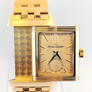 Puede incluir: Un reloj de pulsera dorado con una esfera rectangular y una correa a juego. La esfera presenta una superficie dorada texturizada con manecillas negras y el texto "JAEGER-LECOULTRE". La correa está formada por eslabones rectangulares.