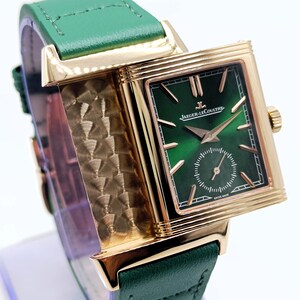 Puede incluir: Un reloj rectangular dorado con esfera verde y correa de cuero verde. La esfera del reloj muestra el texto "Jaeger-LeCoultre" y "Swiss Made". El reloj tiene un peque&ntilde;o dial de segundos y agujas doradas.