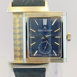 May include: A rectangular Jaeger-LeCoultre watch with a navy blue face and gold hands. The watch has a silver case and a dark blue leather strap. The watch face includes the text "JAEGER-LECOULTRE" and "SWISS MADE".
