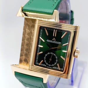 Puede incluir: Un reloj de pulsera rectangular dorado con esfera verde y un peque&ntilde;o dial de segundos. El reloj presenta agujas e indicadores dorados, una correa de cuero verde y el texto "JAEGER-LECOULTRE SWISS MADE".