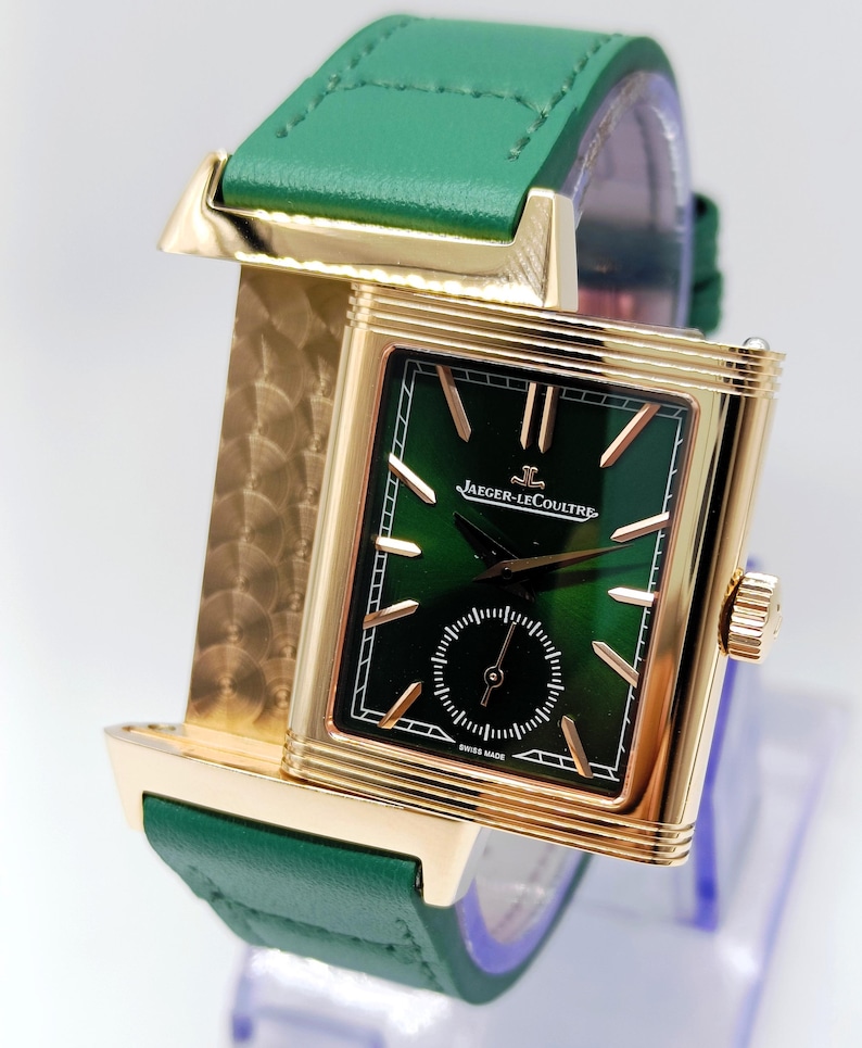 Puede incluir: Un reloj de pulsera rectangular dorado con esfera verde y un peque&ntilde;o dial de segundos. El reloj presenta agujas e indicadores dorados, una correa de cuero verde y el texto "JAEGER-LECOULTRE SWISS MADE".