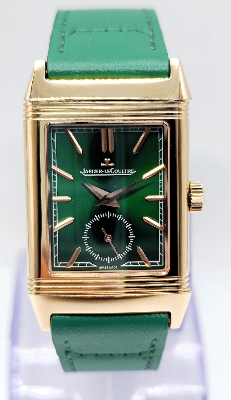 Puede incluir: Un reloj de pulsera rectangular dorado con esfera verde y correa de cuero verde. La esfera del reloj presenta agujas e indicadores dorados, con el nombre de la marca "JAEGER-LECOULTRE". El reloj est&aacute; marcado "SWISS MADE".