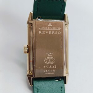 Puede incluir: Reloj Jaeger-LeCoultre Reverso dorado con correa de cuero verde. La esfera del reloj muestra el nombre de la marca y los detalles del modelo. La parte trasera del reloj tiene el texto "3 bar", "1000 hours control" y "Swiss Made".
