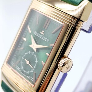 Puede incluir: Un reloj de pulsera rectangular dorado con esfera verde y correa de cuero verde. La esfera del reloj presenta la marca "Jaeger-LeCoultre" y un peque&ntilde;o dial de segundos. El reloj tiene agujas e indicadores de hora dorados.