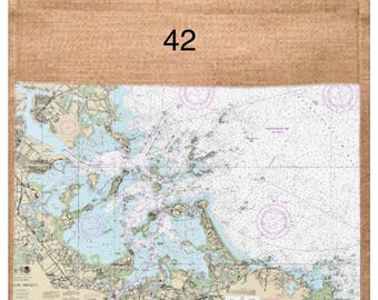 以下が含まれることがあります： 白いハンドルが付いた、天然ジュートのトートバッグ。 ボストンハーバーの海図と座標がプリントされた長方形のパッチが付いています。 上部には数字の「42」が印刷されています。