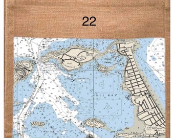 以下が含まれることがあります： 茶色のジュートトートバッグ。海図のデザインで、「Hull Bay」の文字と座標42°17'10" N 70°52'35" Wが描かれています。バッグには数字の「22」がプリントされています。