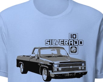 May include: Light blue t-shirt featuring a black and gray graphic of a classic Silverado pickup truck. The text "SILVERADO" and "10" are above the truck image. The shirt has short sleeves and a crew neck.