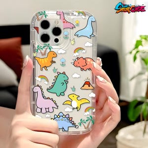 May include: Clear phone case featuring colorful cartoon dinosaurs, rainbows, clouds, and palm trees. The case has a transparent border and a logo in the upper right corner. The case is designed to fit a smartphone.