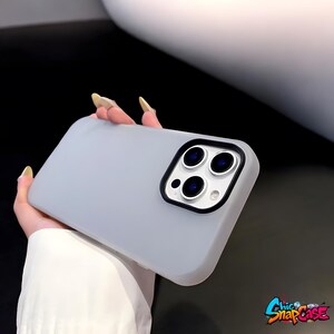 May include: A light gray phone case with a black camera lens border. The case has a matte finish and features the "Chic SnapCase" logo in the bottom right corner. The phone case is held by a person.