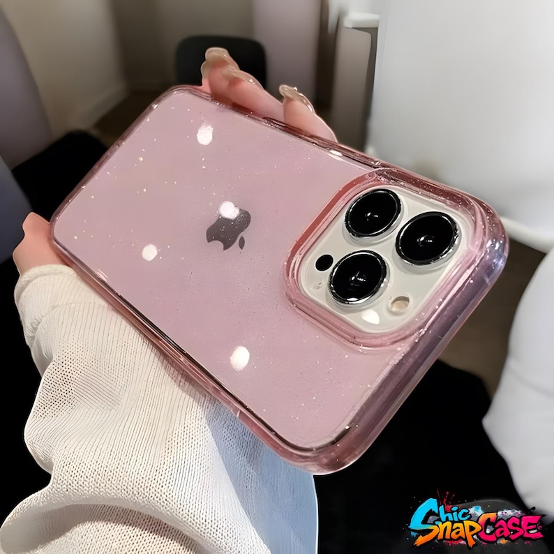 以下が含まれることがあります： ピンク色のグリッターiPhoneケース、透明な縁取り。ケースの背面は透明で、Appleのロゴが見えます。カメラ部分は白い縁取り。右下には「Chic SnapCase」の文字があります。