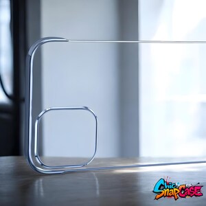 May include: A clear, minimalist phone case with a chrome-like frame. The design features a square element and a curved line, with the text "Chic SnapCase" in a colorful graffiti style at the bottom.
