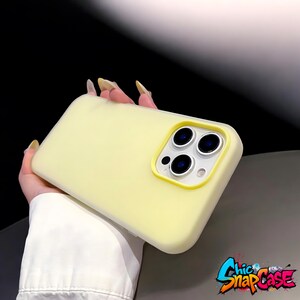 May include: A pale yellow phone case with a camera cutout and a yellow border. The case is held in a hand. The logo "Chic SnapCase" is in the bottom right corner.
