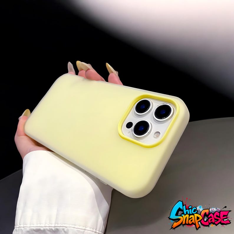 May include: A pale yellow phone case with a camera cutout and a yellow border. The case is held in a hand. The logo "Chic SnapCase" is in the bottom right corner.