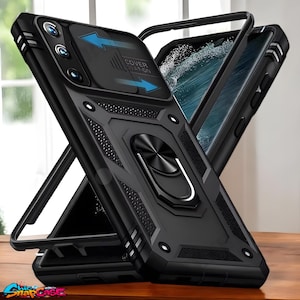 May include: Black phone case with a sliding camera cover and a built-in ring holder. The case has a textured design and the text "COVER STATION" is visible. The phone case is displayed on a wooden surface.