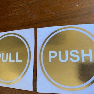 May include: Two gold round stickers with white borders and white text. One sticker says "PULL" and the other says "PUSH".