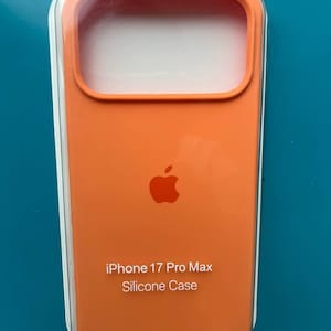 Peut inclure: Une coque de téléphone en silicone orange pour iPhone 17 Pro Max, présentée dans un emballage de vente au détail en plastique transparent. La coque arbore un logo Apple centré dans un ton orange assorti, avec le texte iPhone 17 Pro Max Silicone Case.