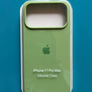 Könnte beinhalten: Eine hellgrüne Silikon-Handyhülle für das iPhone 17 Pro Max in einer transparenten Kunststoffverpackung. Die Hülle zeigt ein zentriertes Apple-Logo und den in Weiß aufgedruckten Text iPhone 17 Pro Max Silicone Case auf der Vorderseite.