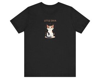 以下が含まれることがあります： 黒いTシャツ。漫画の猫のデザインが特徴です。猫はオレンジ、白、黒の模様で、輝く光で描かれています。「LITTLE DIVA」の文字が猫の上にあります。このシャツは柔らかい素材で作られています。