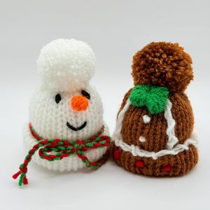 May include: A white knitted snowman hat with a pom-pom, orange nose, and red and green yarn scarf, next to a brown knitted hat with a pom-pom, green bow, and white yarn trim with small red accents, both featuring textured yarn construction.