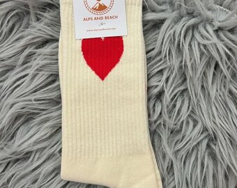 May include: Cream-colored socks with a red heart design. The socks have a ribbed texture and a tag that reads "ALPS AND BEACH". The socks are made of a soft material.