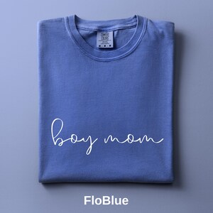 Könnte beinhalten: Ein kornblumenblaues Kurzarm-T-Shirt mit dem Schriftzug "boy mom" in weißer Schreibschrift auf der Brust. Das T-Shirt hat einen Rundhalsausschnitt und ein aufgedrucktes Comfort Colors Markenetikett im inneren Kragenbereich.