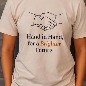 May include: Beige t-shirt with a black line drawing of two hands shaking. The text "Hand in Hand, for a Brighter Future" is printed below the graphic in black and orange.
