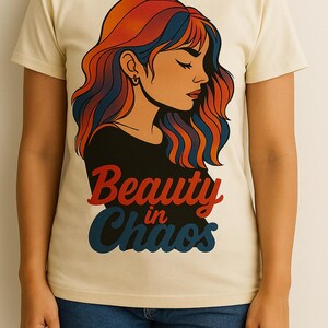 Peut inclure: T-shirt crème avec un graphisme de femme aux cheveux rouges, oranges et bleus. Le texte "Beauty in Chaos" est imprimé en rouge et bleu. Le t-shirt est porté avec un short en jean.