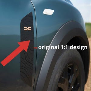 Può includere: Un'auto verde acqua con un pannello nero con un motivo a venature del legno e le lettere "DC" color rame. È visibile anche il testo "original 1:1 design".