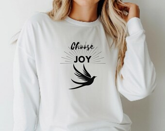 Könnte beinhalten: Weißes Langarmshirt mit dem Schriftzug "Choose JOY" in schwarzer Schrift und einer schwarzen Vogelgrafik. Das Design zeigt einen Sonnenaufgangseffekt hinter dem Wort JOY. Das Shirt ist aus weichem Material.