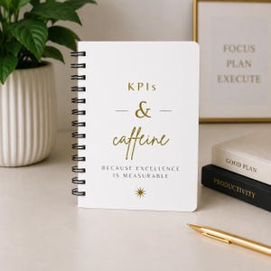 Może przedstawiać: Biały notatnik ze spiralą i złotym napisem KPIs & caffeine, po którym następuje tekst BECAUSE EXCELLENCE IS MEASURABLE oraz mała złota ikona gwiazdki. Okładka ma przejrzysty design z czarną spiralą po lewej stronie notatnika.